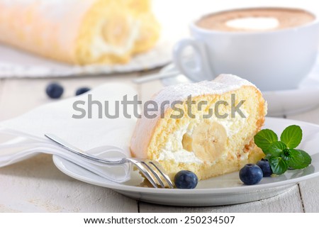 Swiss roll stuffed with banana and cream, a cup of cappuccino in the background