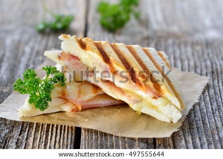 Pressed and toasted double panini with ham and cheese served on sandwich paper on a wooden table