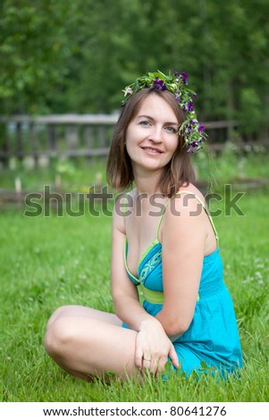 young women with flower diadem sit on grass