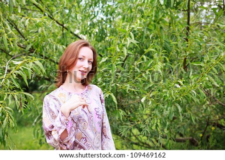 Portrait of a beautiful European woman in a lilac dress with patterns on a background of green trees.