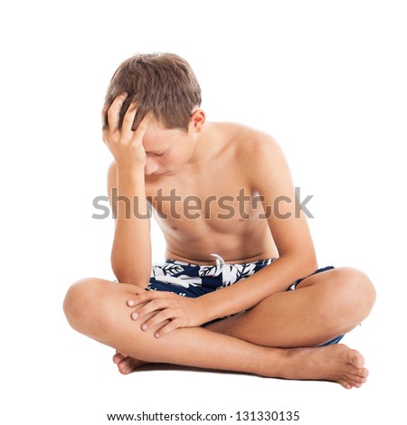 Portrait of a cute european teen boy wearing swimming shorts. A boy sitting on the floor. Studio shot, isolated on white background.