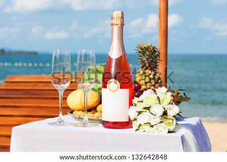 Wedding dinner on a sandy beach. Lounger and a table with fruit and bottle of wine.