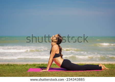Beautiful young woman is doing yoga near the sea. Pose dog muzzle up.
