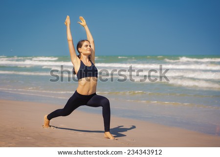 Beautiful young woman is doing yoga near the sea. Warrior pose.