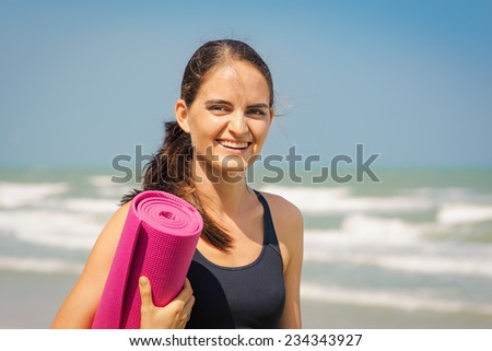 Beautiful young woman is going to do yoga. Portrait with red yoga carpet on the sea background.