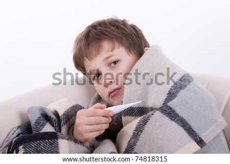 The sick boy covered by a checkered plaid, holds a thermometer in a hand