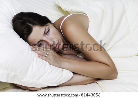 A sad young woman lying on white bed on a pillow