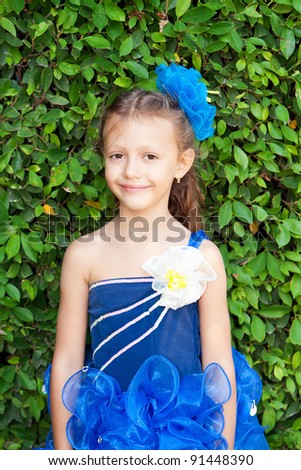 Portrait of a pretty girl with long hair and a bow in a smart blue dress on green background