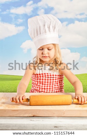 Little girl in chef hat cook healthy soup in a big pot, and prepares the dough for dumplings, pizza, using a wooden rolling pin - in the open air on the background of the solar sky  - picnic
