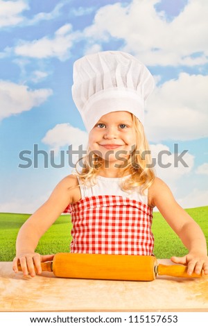 Little girl in chef hat cook healthy soup in a big pot, and prepares the dough for dumplings, pizza, using a wooden rolling pin - in the open air on the background of the solar sky  - picnic