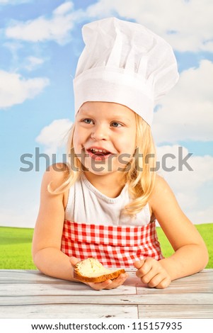 laughing pretty little girl in a cap with a basket chef bread, bread them, a slice of buttered chlebka heart-shaped cake - against a blue sky.
