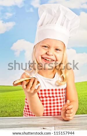 laughing pretty little girl in a cap with a basket chef bread, bread them, a slice of buttered chlebka heart-shaped cake - against a blue sky.