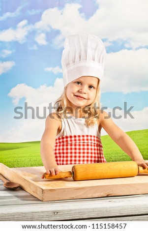 little girl in a chef\'s hat on a sky background makes dough for dumplings, pizza with a rolling pin