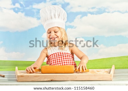 little girl in a chef\'s hat on a sky background makes dough for dumplings, pizza with a rolling pin