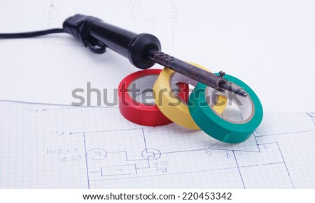 A soldering iron and adhesive plastic tape on the background on the electric scheme