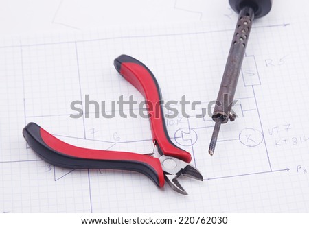 Metal nippers and soldering iron on a background of the electric scheme