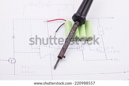 Soldering iron and batteries on the background of the electric scheme