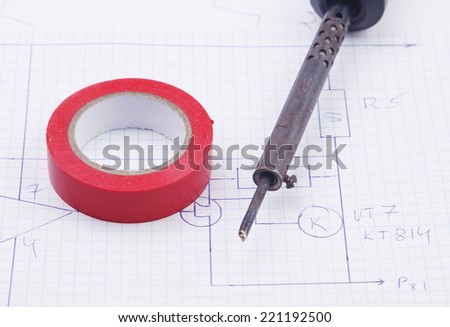A soldering iron and adhesive plastic tape on the background of the electric scheme