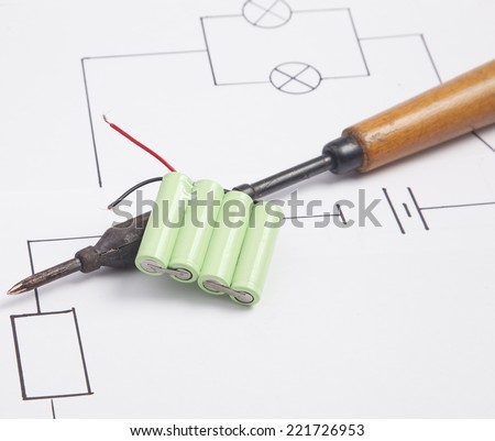A soldering iron and battery on a background of the electric scheme
