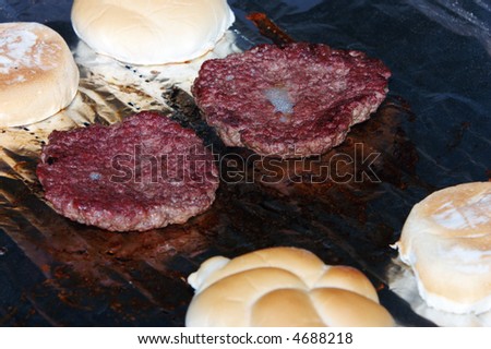 Sizzling burgers and toasting buns on the grill.  Shallow DOF. Focus on front of upper right patty