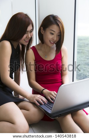 Two young Asian ladies, looking at their laptop working.