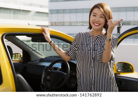 A young Asian lady holding car keys with her yellow car.