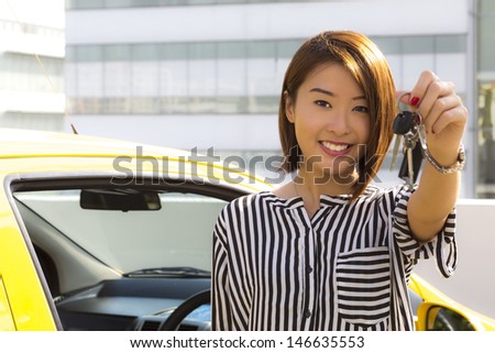 A charming Asian lady standing in front of her car showing her car keys.