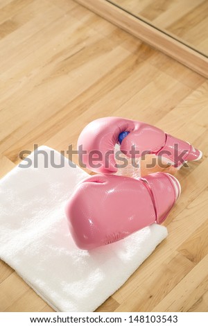A vertical shot of a pair of pink boxing gloves with a towel and drinking bottle in a gym.