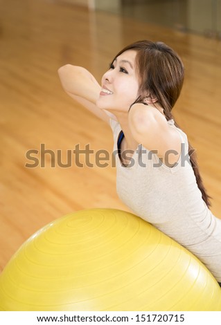 An Asian lady doing her warm up stretching exercise with a ball in a gym