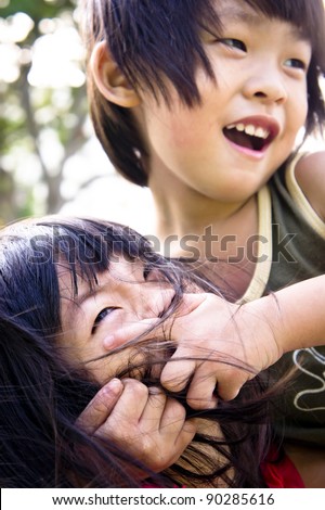 A playful Asian boy covering his sister\'s mouth not allow her to speak.