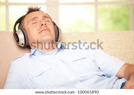 Man listening music with cordless headphones sitting on sofa at home
