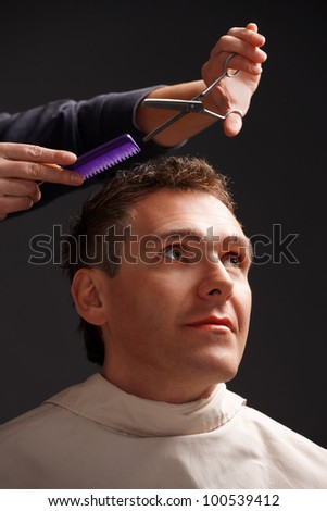 Barber cutting hair with scissors and comb, a client is a young caucasian man