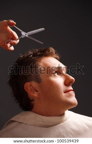Barber cutting hair with scissors, a client is a young caucasian man