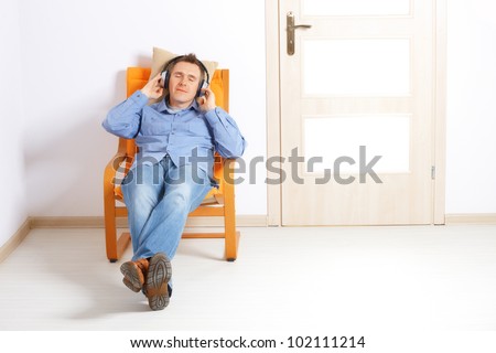Man listening music with headphones sitting at home and smiling.