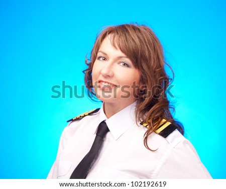 Beautiful woman pilot wearing uniform with epauletes standing on blue background.