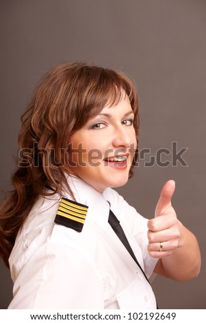 Beautiful airline pilot wearing uniform with epauletes showing thumb up gesture of approval
