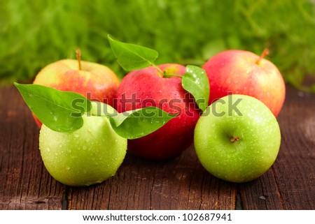 Five fresh wet apples with leaves on wooden board. Two green and three red.