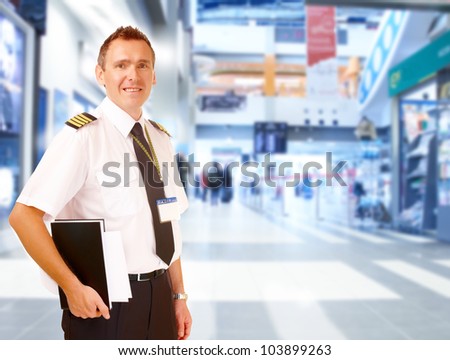 Airline captain pilot wearing uniform with epaulettes standing at airport with his flight documents.