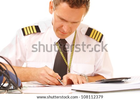 Airline pilot wearing shirt with epaulets and tie filling in and checking papers flight plan, weather forecast. Headset on the table.