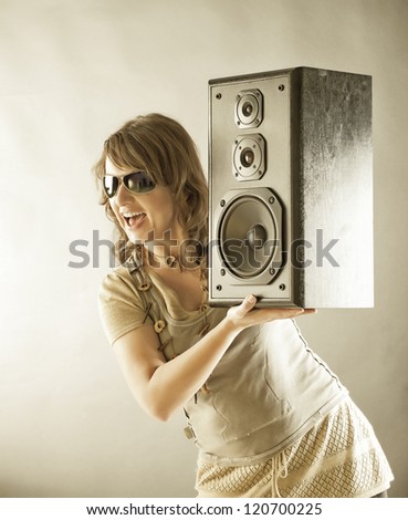 Young beautiful smiling woman with sunglasses holding big wooden speaker and listening music