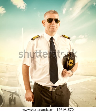 Cheerful pilot wearing uniform with epaulettes, standing with airliner in background.