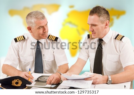 Two airline pilots preparing to flight, checking papers flight plan, log book. Pilots are sitting in AIS ARO Air Traffic Services Reporting Office