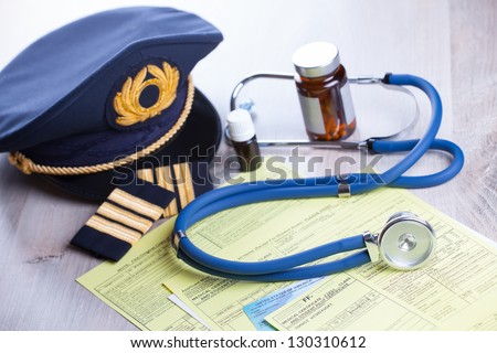 Close up of an airplane pilot equipment hat and epaluetes with doctor\'s stethoscope, forms, medical and pilot certificate and drugs. Conceptual image of medical exam.