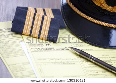 Close up of an airplane pilot equipment hat and epaluetes with medical forms and pen. Conceptual image of medical exam.