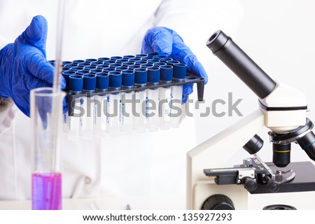 Lab technician holding test tubes filled with colored fluid, chemical flasks and microscope in background