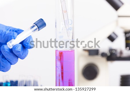 Lab technician working with equipment: microscope, test tubes  filled with colored fluid, chemical flasks