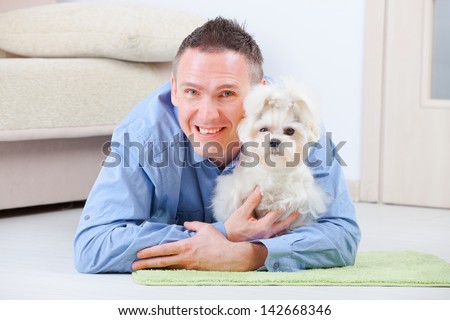 Little dog maltese laying with his owner on the floor in home