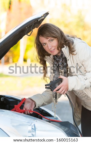 Beautiful woman connecting booster cables to a car battery