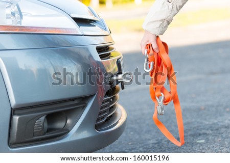 Hand holding tow rope near towing hook assembled to a broken car