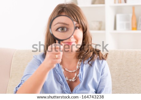 Beautiful woman holding loupe or magnifying glass on her eye